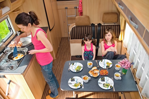 Family eating together in RV interior, mother and kids travel in motorhome on family vacation with children