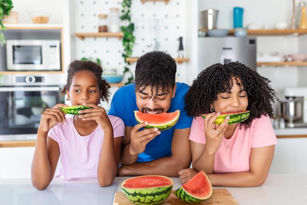 Family eats a sweet watermelon in the kitchen A man and a woman with daughter eat a ripe watermelon in the kitchen Happy family eating watermelon