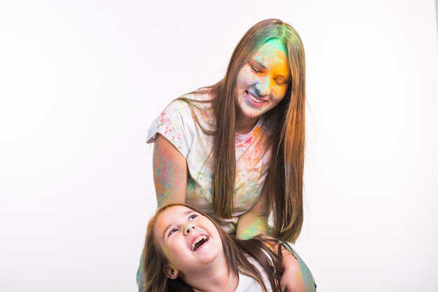 Family, festival of holi and holidays concept - Woman and little smiling girl covered with colourful powder over white surface