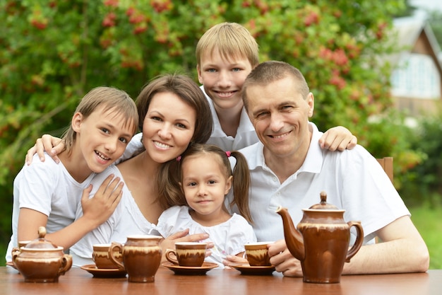 Family of five drinking tea at table outdoors in summer time