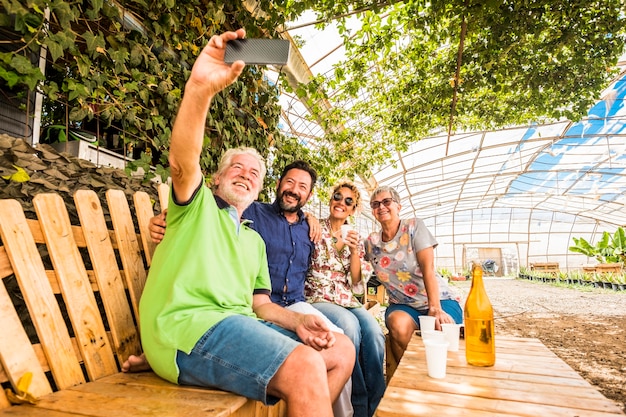 Family and friends have fun all together in outdoor leisure activity sit down on a recycled wooden bench and taking picture selfie with smartphone