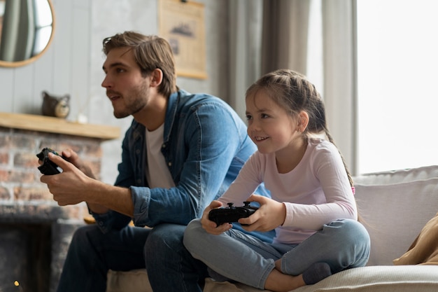 Family, gaming and entertainment concept - happy father and little daughter with gamepads playing video game at home.