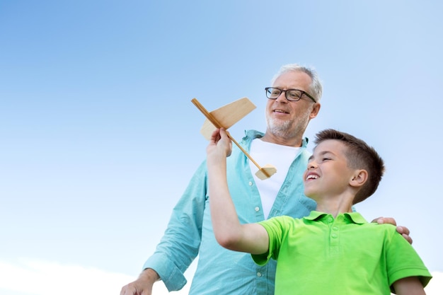 family, generation, future, dream and people concept - happy grandfather and grandson with toy airplane over blue sky