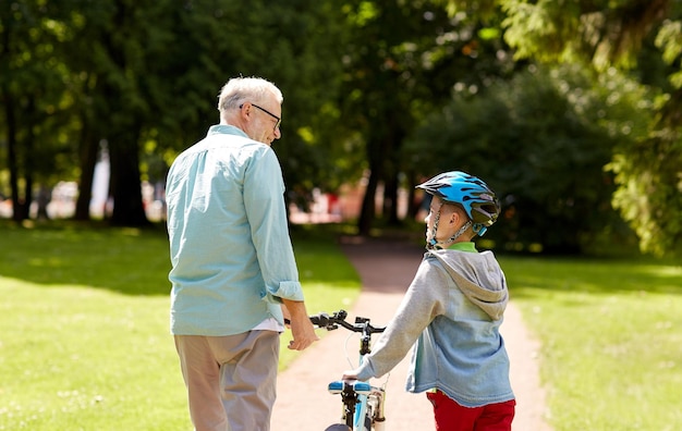 family, generation, safety and people concept - happy grandfather and boy with bicycle and bike helmet talking at summer park