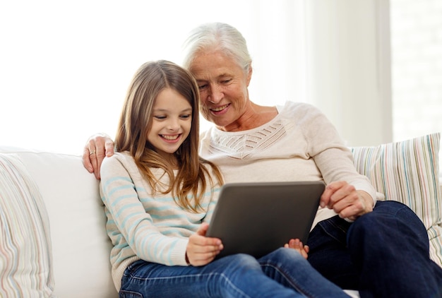 family, generation, technology and people concept - smiling granddaughter and grandmother with tablet pc computer sitting on couch at home