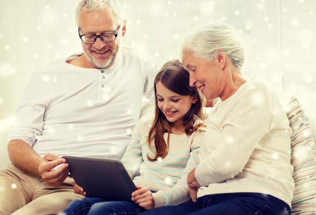 family, generation, technology and people concept - smiling grandfather, granddaughter and grandmother with tablet pc computer sitting on couch at home