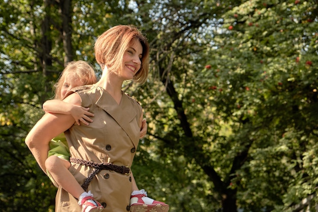 Family happiness. Cute young daughter riding her mom's back, on the nature in the park