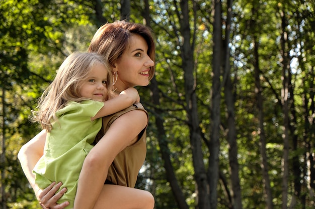 Family happiness. Cute young daughter riding her mom's back, on the nature in the park