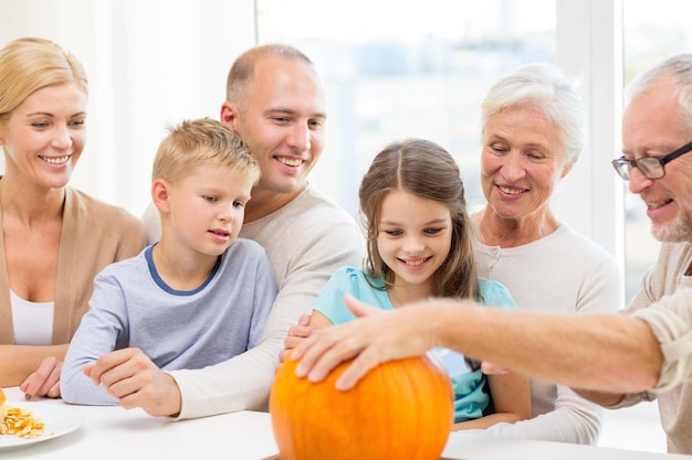 family, happiness, generation, holidays and people concept - happy family making halloween pumpkins at home