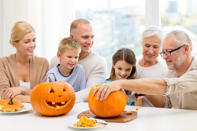 family, happiness, generation, holidays and people concept - happy family making halloween pumpkins at home