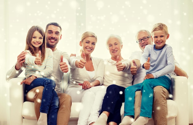 family, happiness, generation and people concept - happy family sitting on couch and showing thumbs up gesture at home