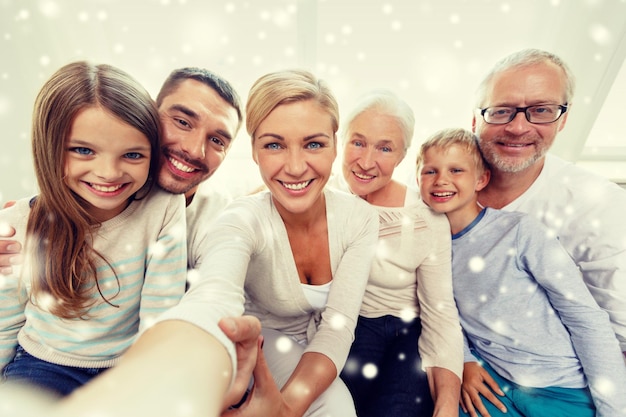 family, happiness, generation and people concept - happy family sitting on couch and taking selfie with camera or smartphone at home