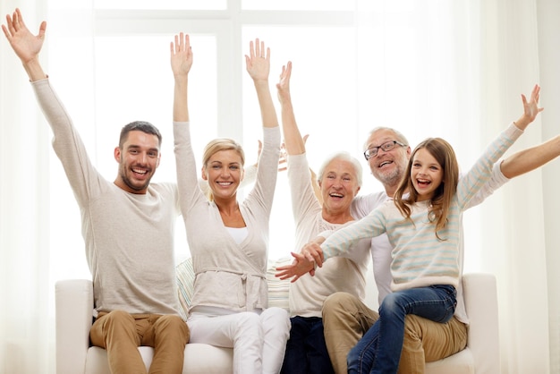 family, happiness, generation and people concept - happy family sitting on sofa and rising hands at home