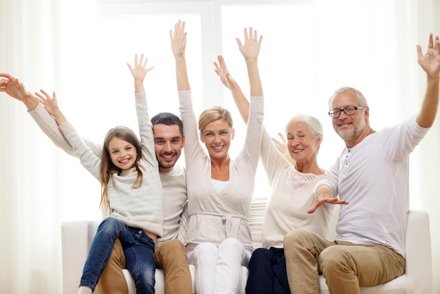 family, happiness, generation and people concept - happy family sitting on sofa and rising hands at home