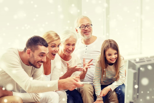 family, happiness, generation and people concept - happy family sitting on sofa and watching tv at home