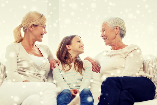 family, happiness, generation and people concept - smiling mother, daughter and grandmother sitting on couch at home