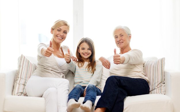 family, happiness, generation and people concept - smiling mother, daughter and grandmother sitting on couch at home