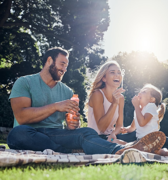 Family happy and bubbles with picnic in park together for summer relax and nature Smile spring and peace with parents playing with girl in countryside field for youth lifestyle and happiness