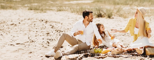 Family Having Summer Picnic Sitting On Blanket Talking In Countryside