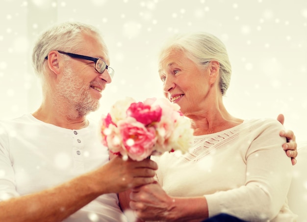 family, holidays, age and people concept - happy senior couple with bunch of flowers at home