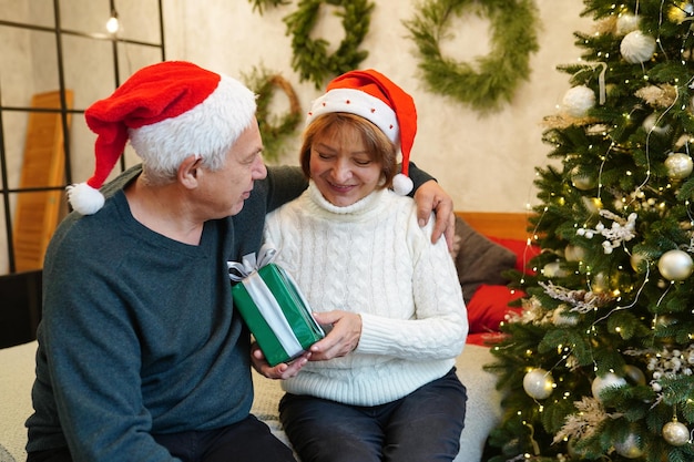 Family, holidays, age and people concept - happy senior couple with gift box in living room near christmas tree