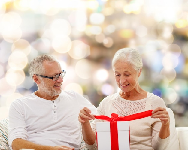 family, holidays, christmas, age and people concept - happy senior couple with gift box over lights background