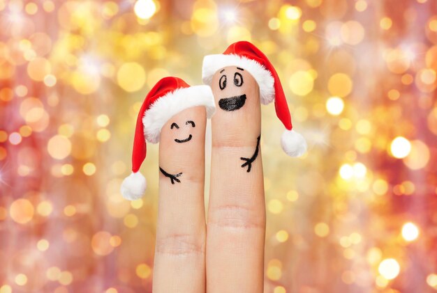 family, holidays, christmas and body parts concept - close up of two fingers with smiley faces and santa hats over lights background