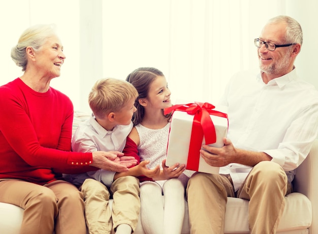 family, holidays, generation, christmas and people concept - smiling grandparents and grandchildren with gift box sitting on couch at home