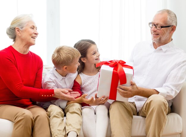 family, holidays, generation, christmas and people concept - smiling grandparents and grandchildren with gift box sitting on couch at home