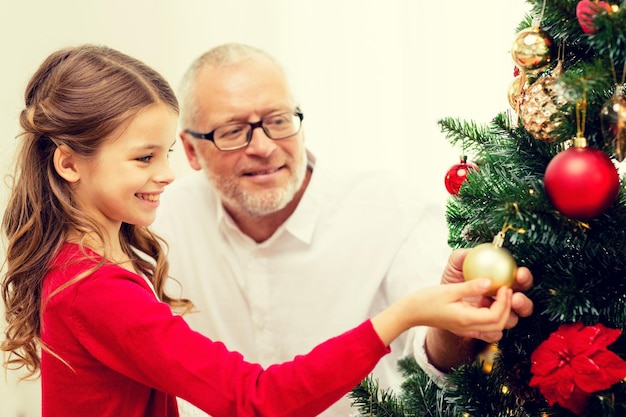 family, holidays, generation and people concept - smiling girl with grandfather decorating christmas tree at home