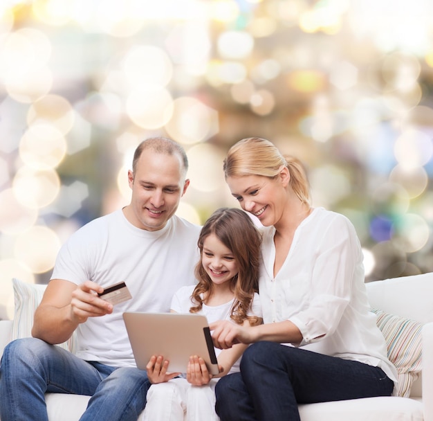 family, holidays, shopping, technology and people - smiling mother, father and little girl with tablet pc computer and credit card over lights background