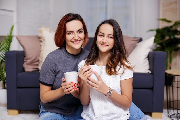 Family and home concept - portrait of happy mother and daughter sitting in living room and drinking tea