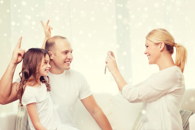 family, home, technology and people - happy family with camera taking picture over snowflakes background