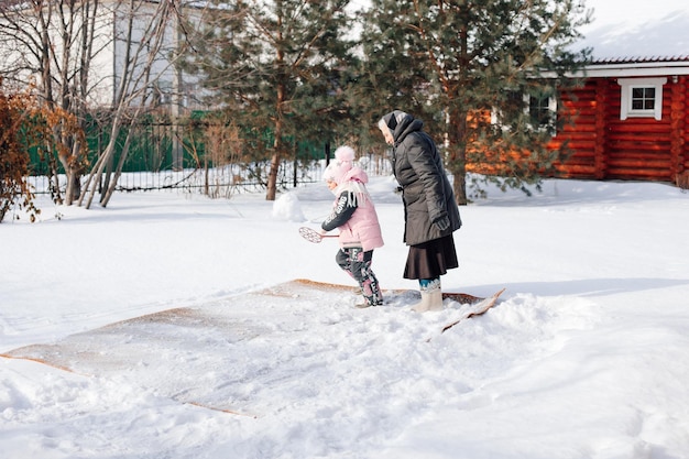 Family is cleaning carpet in backyard Caucasian woman and child traditionally clean carpet with fresh snow and carpet beater near wooden cottage in winter side view