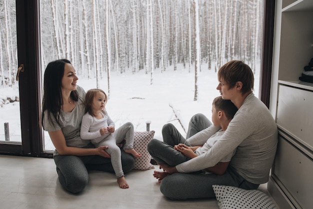 The family is sitting at the window and looking at the winter forest. Good New Year spirit. Morning in pajamas.