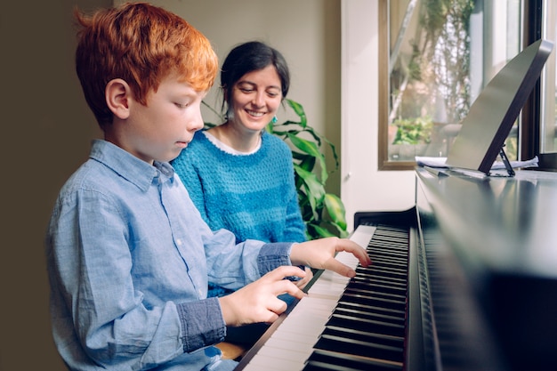 Family lifestyles with children. Educational activities at home. Young red hair kid playing the piano. Little boy rehearsing music lessons on a keyboard at home. Study and learn music career concept.