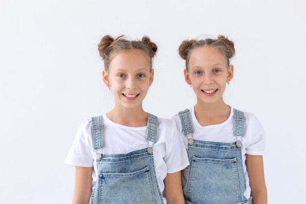 Family and love concept - two smiling twin sisters hugging over white wall.