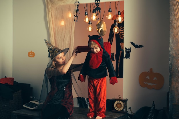 Family love and Halloween party Close up shot of blond mom with little dressed boy creepy costumes eyewear and head wear gesturing boo in decorated nice light halloween room indoors