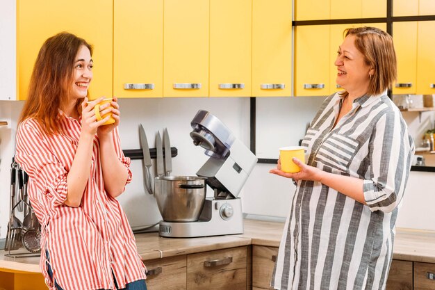 Family morning Mother and daughter drinking coffee chatting having fun in modern kitchen at home