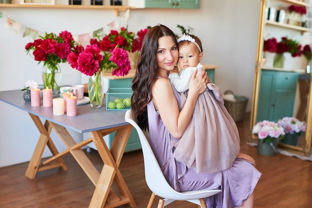 Family mother and daughter with peonies flowers in kitchen at home. Happy mother and baby daughter. Happy family. 