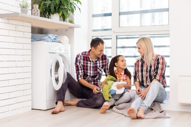 Photo family mother, father and child girl little helper in laundry room near washing machine and dirty clothes