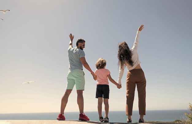 Family of mother father and kid boy looking in future holding hands in summer back view adoption