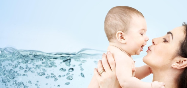 family, motherhood, people and child care concept - happy mother kissing adorable baby over blue background with water splash