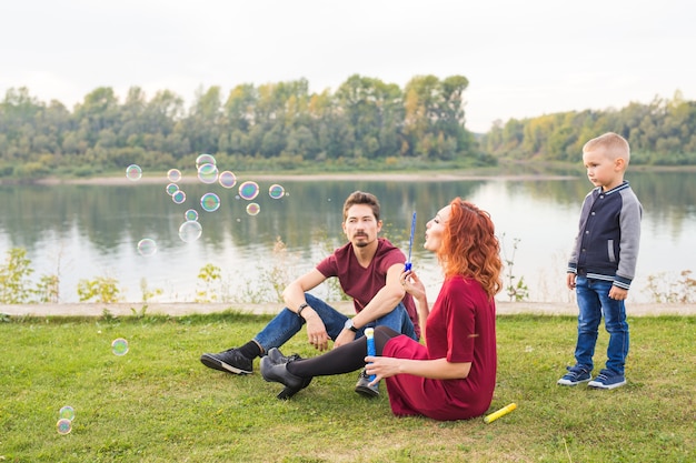 Family and nature concept - Mother, father and their child playing with colorful soap bubbles