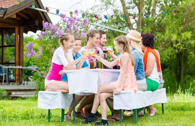 Family and neighbors at garden party drinking, sitting in front of a home with friends and family