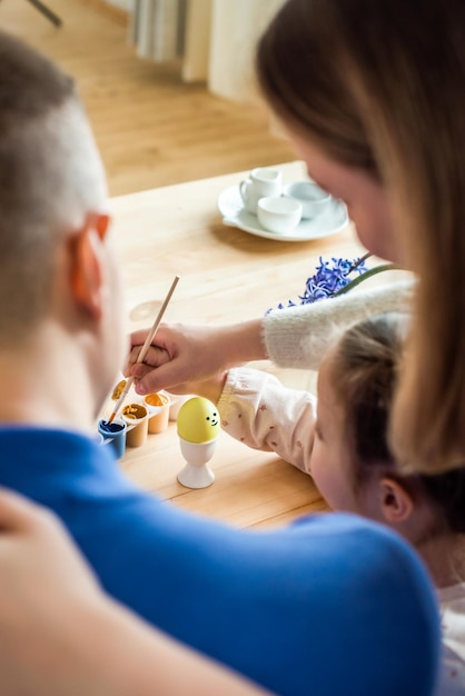 The family paints colorful Easter eggs mom dad and daughter celebrate spring holiday together young woman man and girl coloring traditional scenery