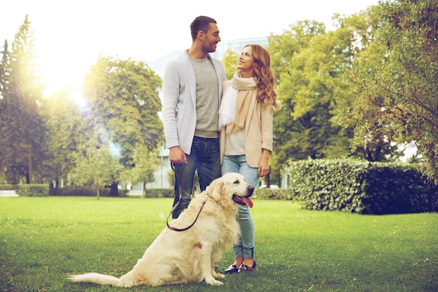 family, pet, animal and people concept - happy couple with labrador retriever dog walking in city park