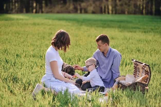 Family on a picnic in the forest. In the meadow. Picnic basket with food. The dog runs and wants to play. A child with glasses. Blue color in clothes. To eat outdoors. Time with family.