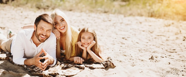 Family picnic parents and daughter lying on blanket smiling to camera on summer day outdoors after