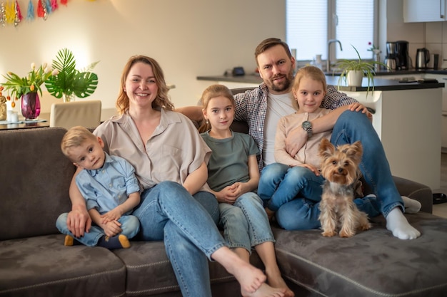 Family portrait family photo in which mom dad daughters son and dog are smiling and hugging on the couch in a cozy homely atmosphere selective focus